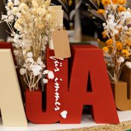Dekorative Holzbuchstaben in Beige und Rot, die das Wort „JA“ formen, verziert mit Trockenblumen und dem Schriftzug „für immer“.