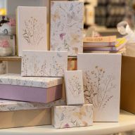 Geschenkboxen in verschiedenen Größen mit Blumen- und Schmetterlingsmustern, neben Hochzeitsfiguren