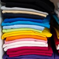 Zwei ordentliche Stapel farbiger T-Shirts nebeneinander in einem Schrankfach.